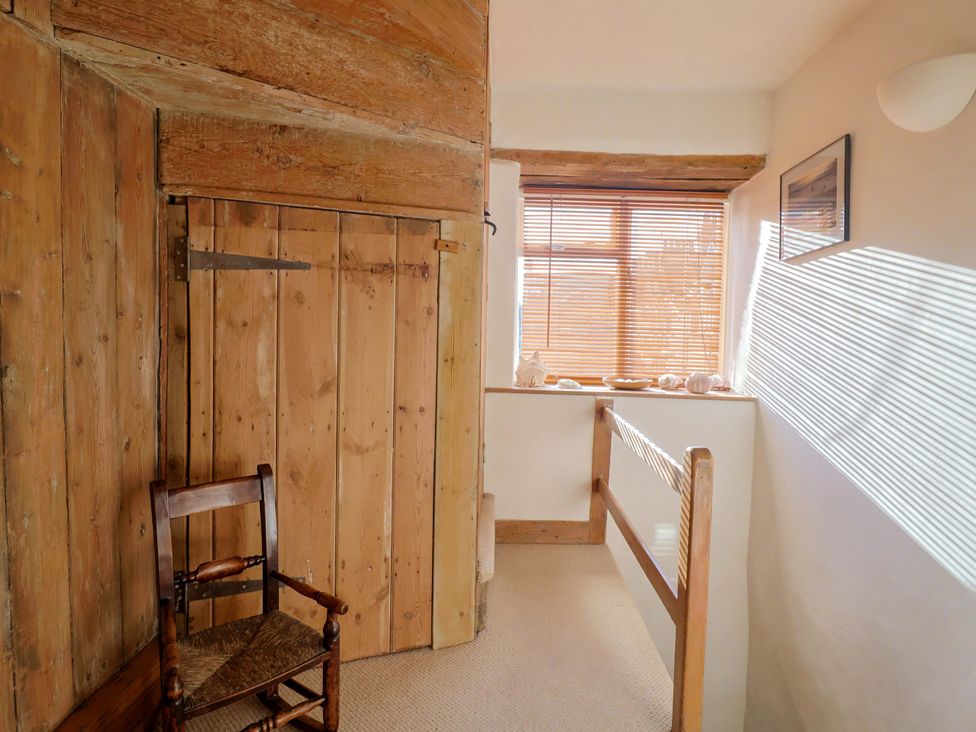 A hallway with a wooden chair and window at Rope Cottage in Bridport