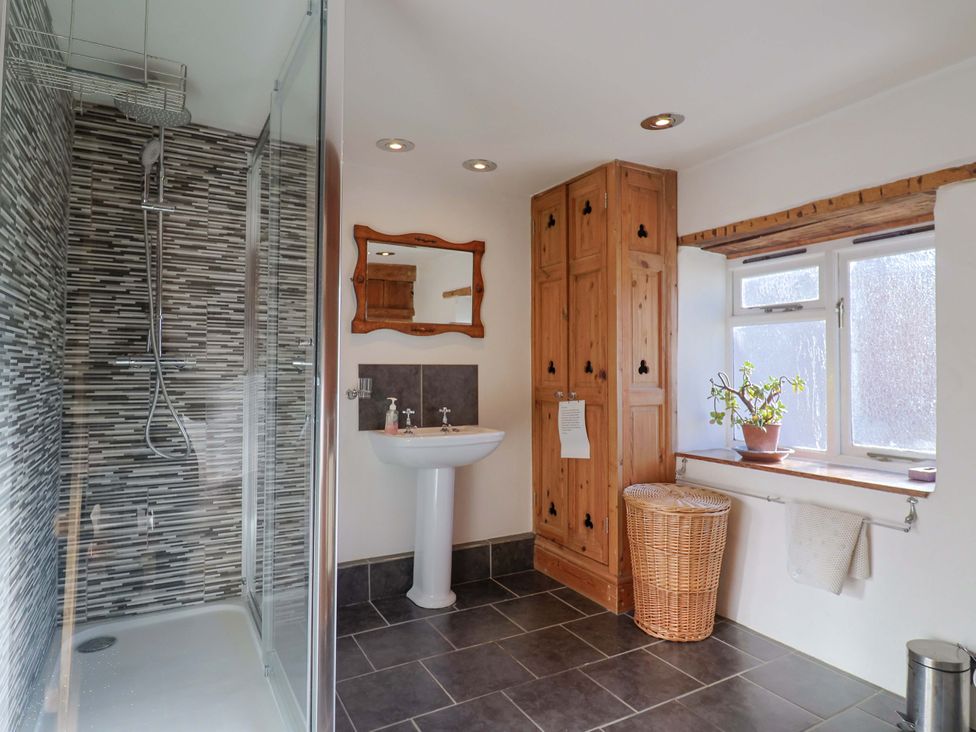 A bathroom with a shower, sink, and wooden cabinet at Rope Cottage in Bridport