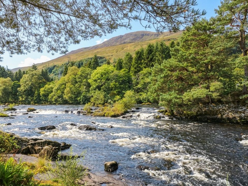 A river with rocks and trees near a mountain at Glen Lochay Lodge in Killin