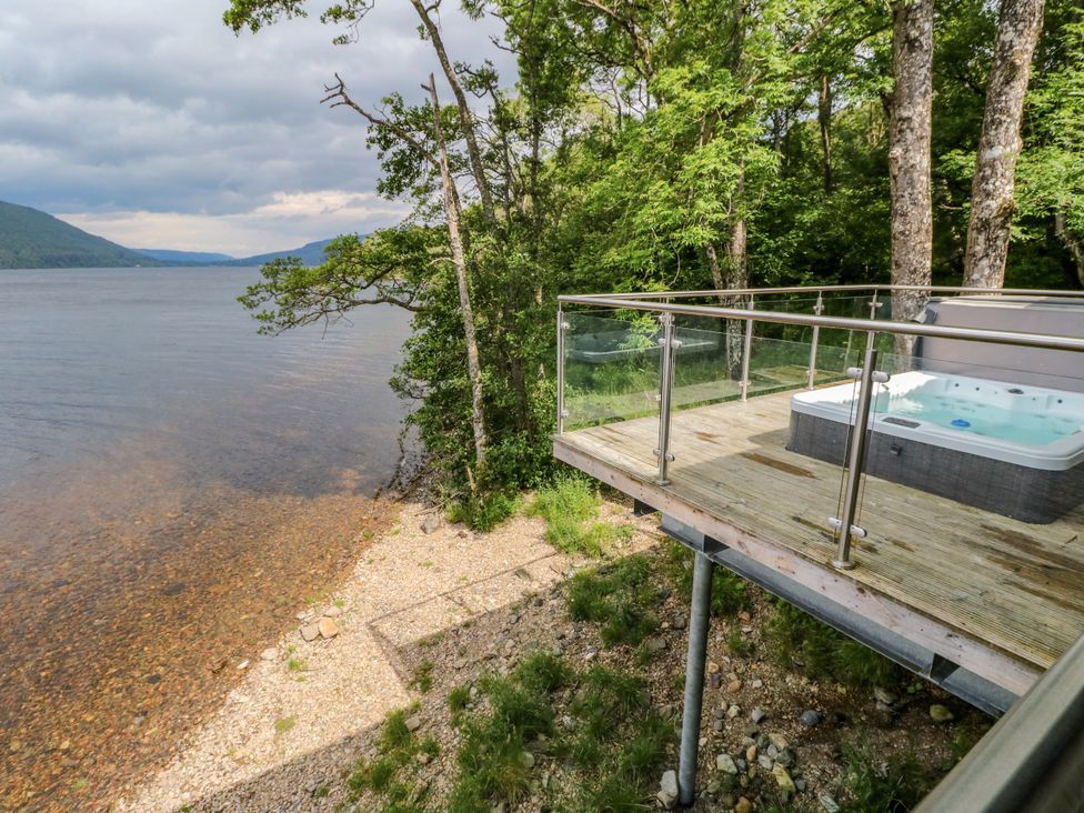 An outdoor deck with a hot tub overlooking a lake at Osprey Boathouse in Killin