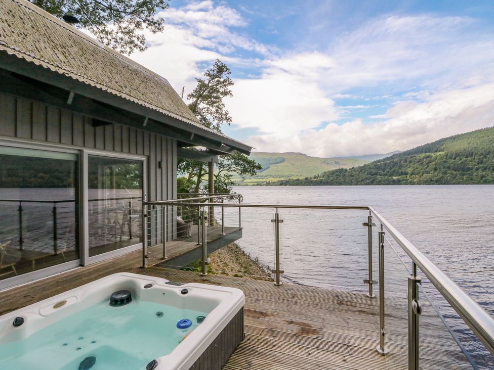 An outdoor area with a hot tub overlooking a lake at Osprey Boathouse Killin