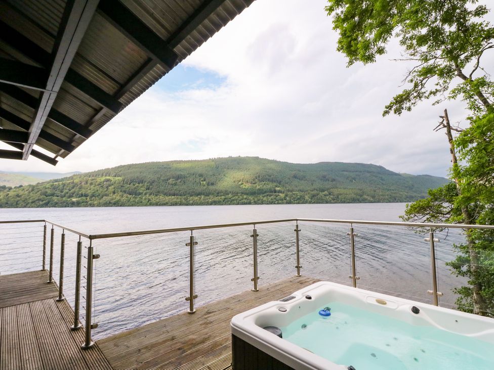 An outdoor deck with a hot tub overlooking the water at Osprey Boathouse in Killin
