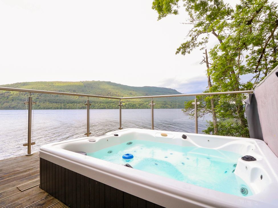 An outdoor area with a hot tub overlooking water and mountains at Osprey Boathouse in Killin