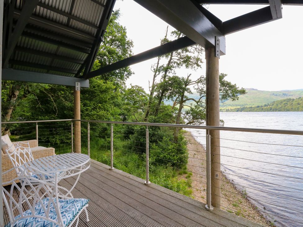A deck overlooking a lake with a table and chairs at Osprey Boathouse in Killin
