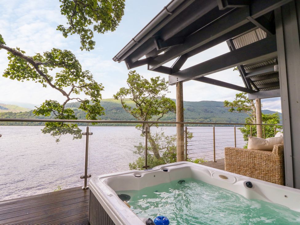 An outdoor area with a hot tub and seating overlooking the lake at Dipper Boathouse in Killin