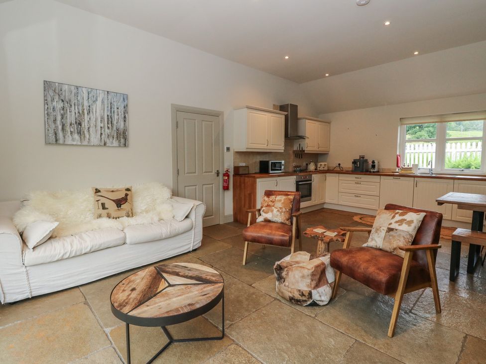 A living room with a sofa and a kitchen area at Ghillie's Cottage in Killin