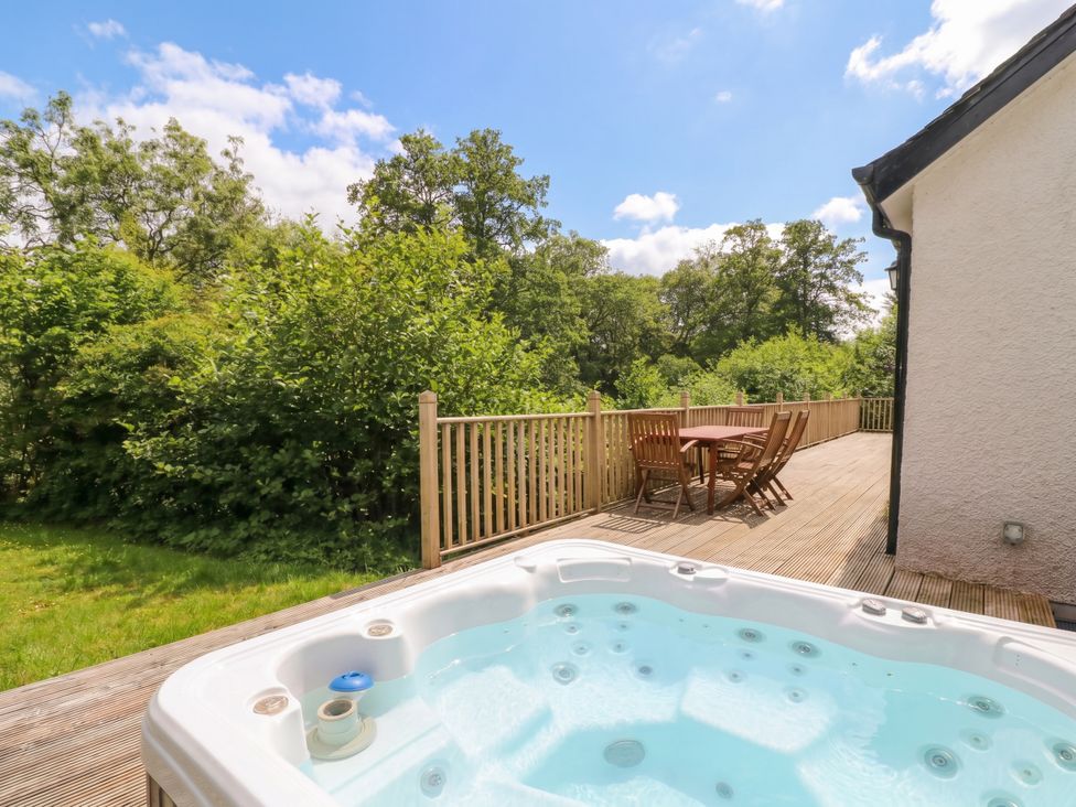 A hot tub on a deck with a table and chairs surrounded by greenery at Ghillie's Cottage in Killin