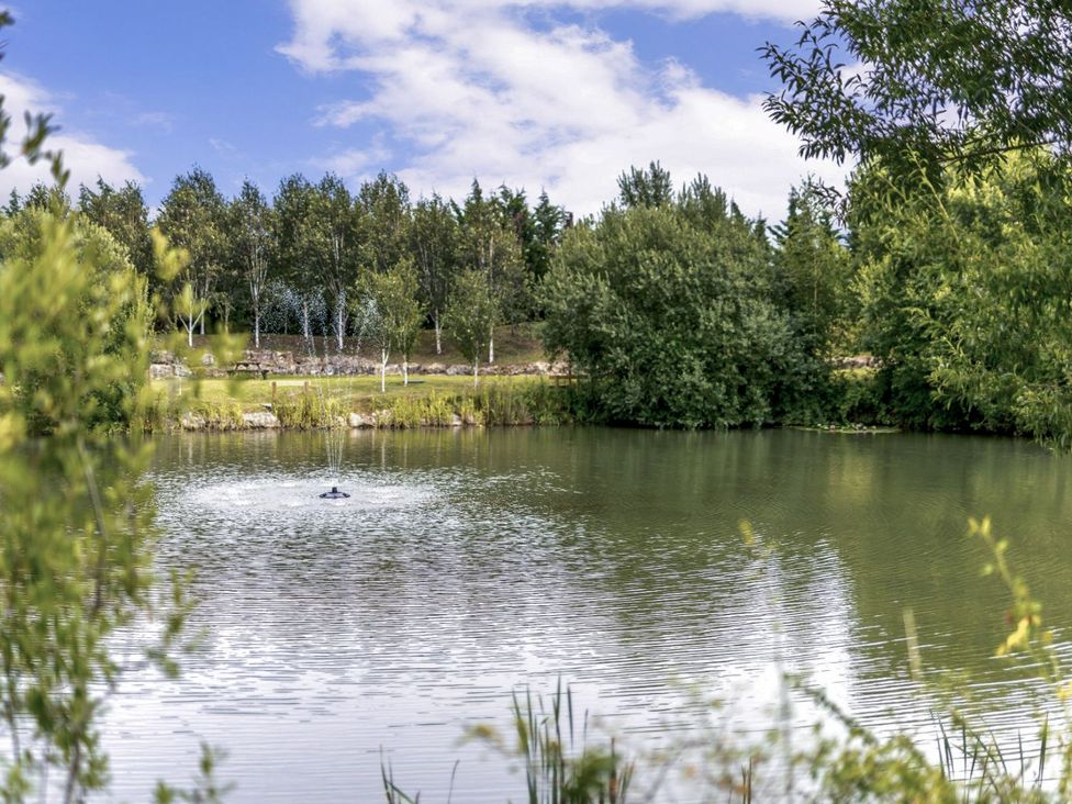 A pond with a fountain and trees at The Castor in Kings Cliffe