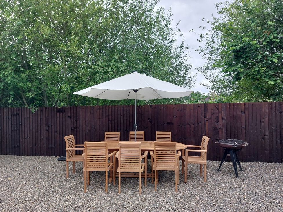 A garden with a wooden table and chairs under a parasol at 1 Clarkes Lane St Martins