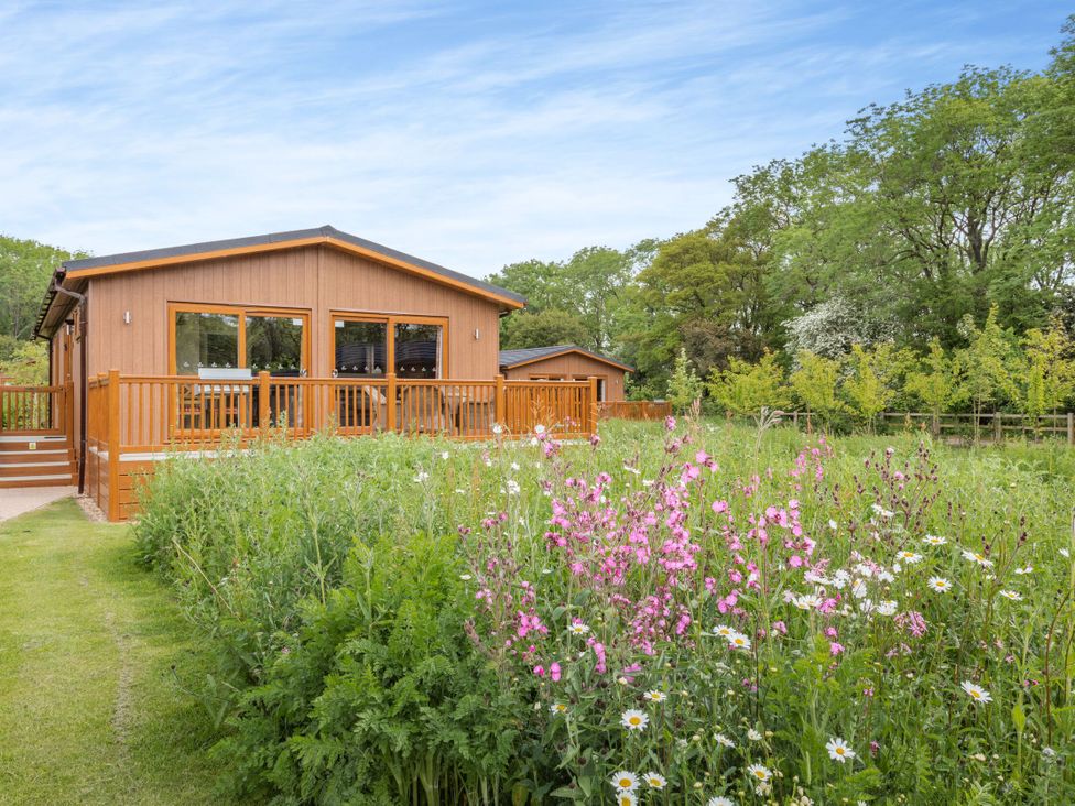 A cabin with a deck surrounded by a flower garden at The Sutton in Kings Cliffe