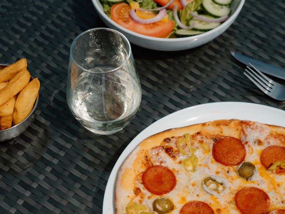 An outdoor dining area with a pizza, salad, glass of water, and potato wedges at The Sutton (Pet) Kings Cliffe
