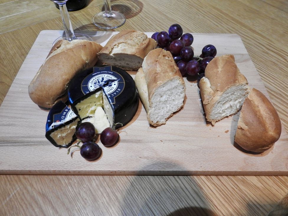 A cheese, bread, and grapes on a cutting board at Ramsgrove in Swansea