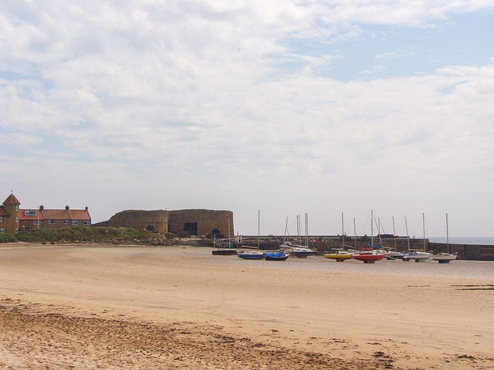 A beach with boats moored at a pier at Beadlin cottage in Beadnell