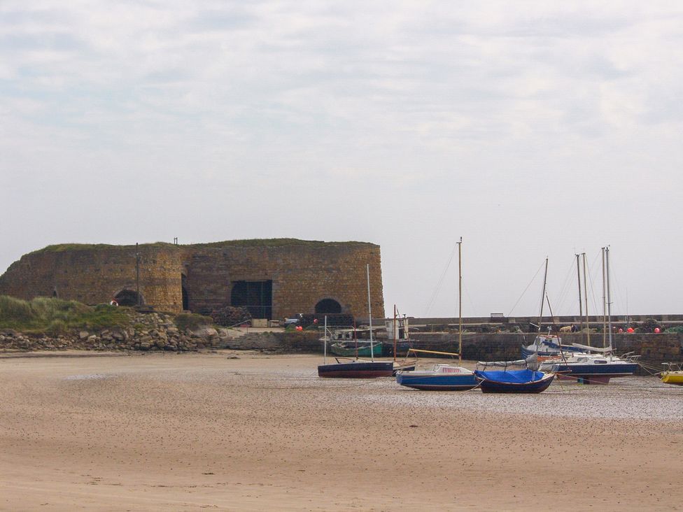 Boats near a stone building and pier at Beadlin cottage Beadnell