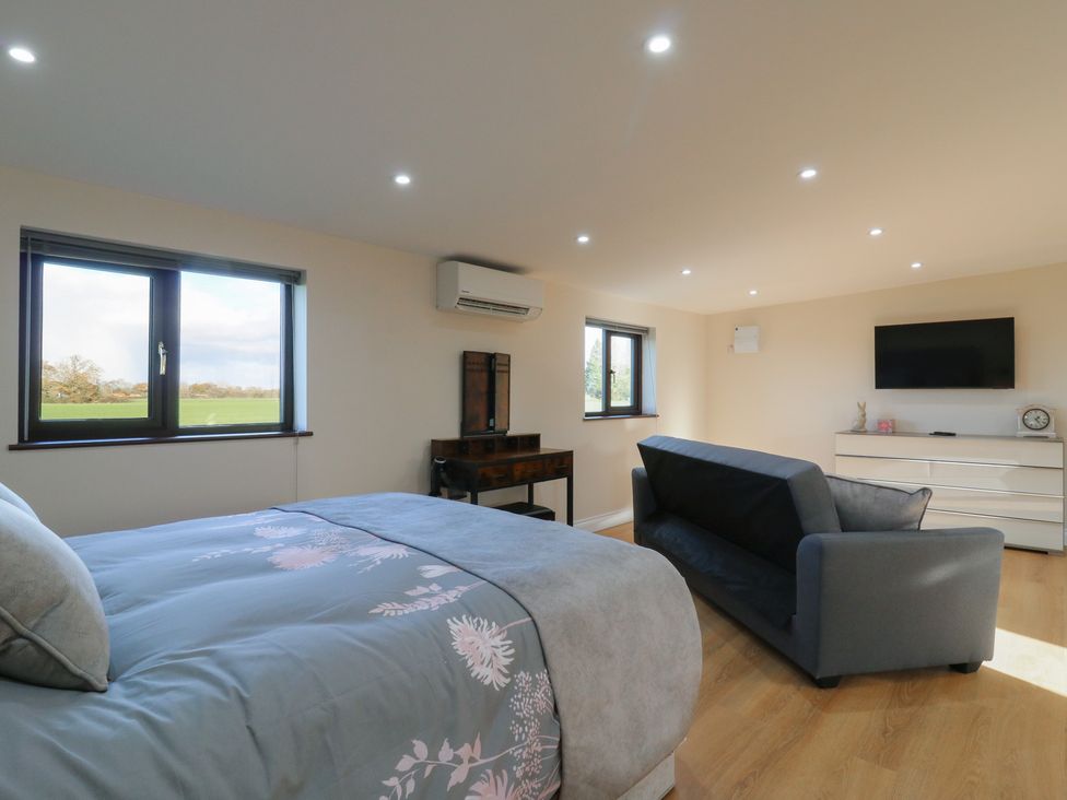 A bedroom with a bed, sofa, and television at Aloe Lodge in Diss