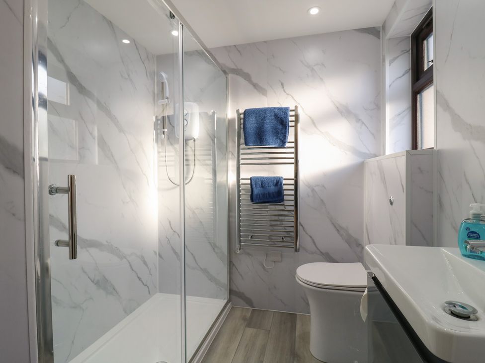 A bathroom with a shower, toilet, sink, and towel warmer at Aloe Lodge in Diss