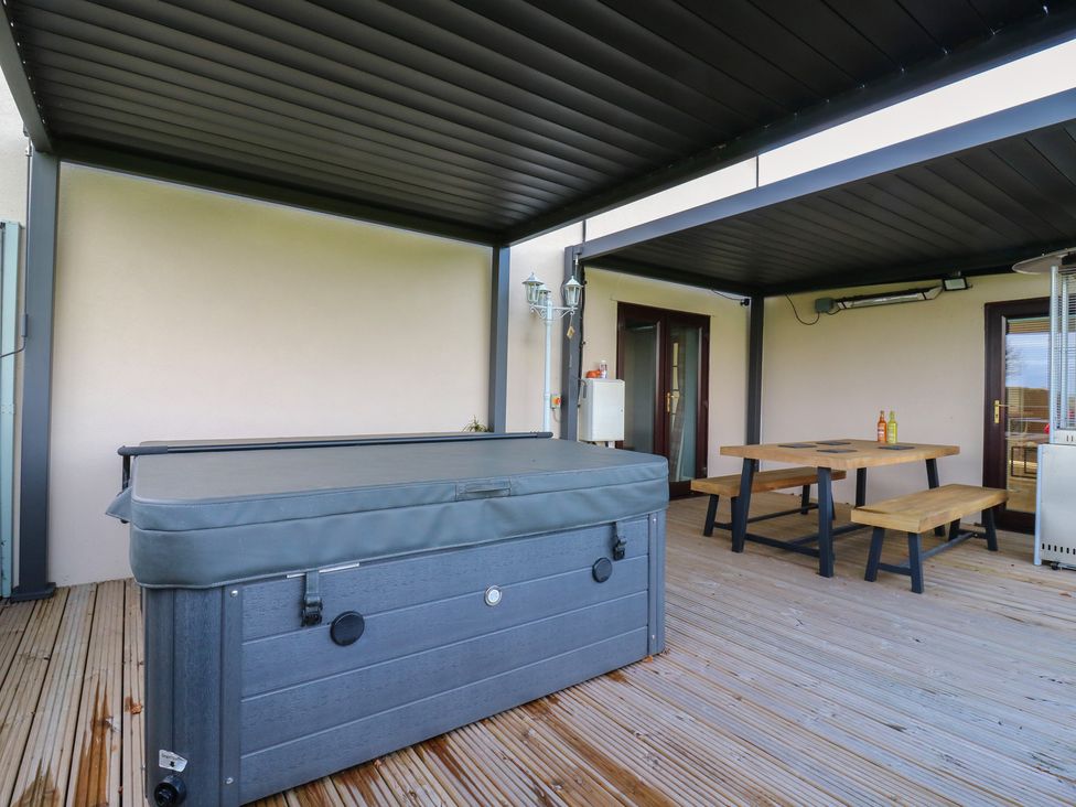 An outdoor patio with a hot tub and dining table at Aloe Lodge in Diss