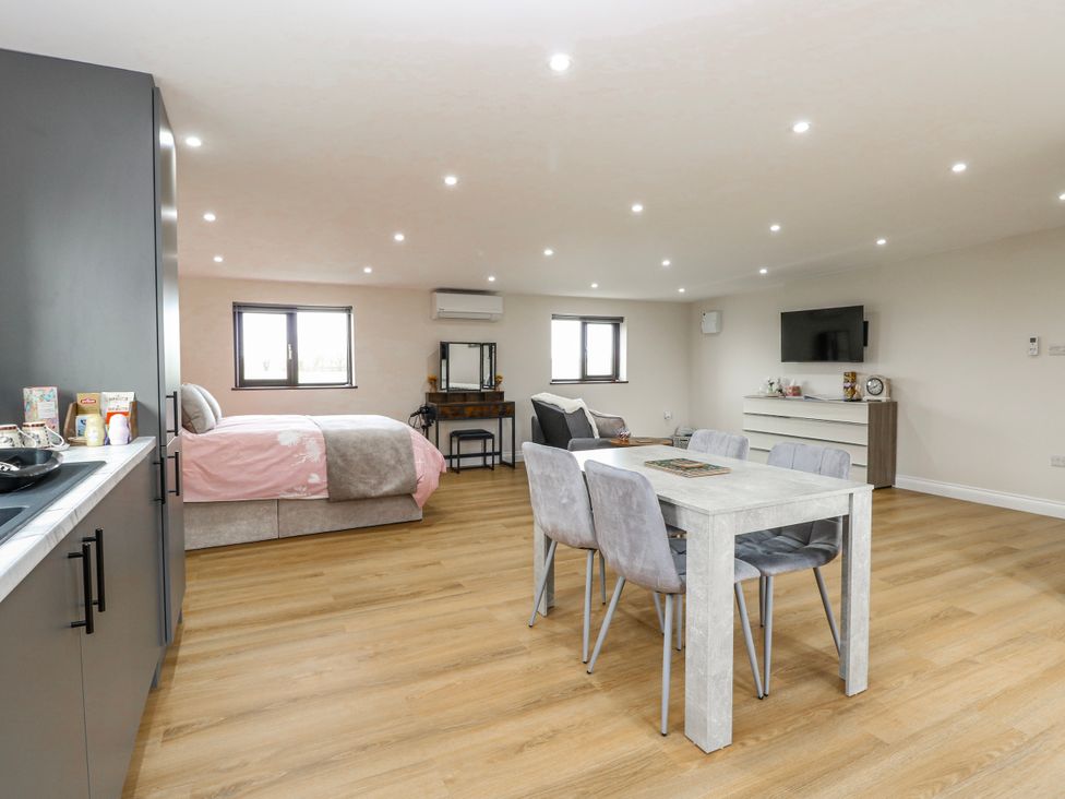 A studio apartment featuring a bed, dining table with chairs, and a TV at Aloe Lodge in Banham