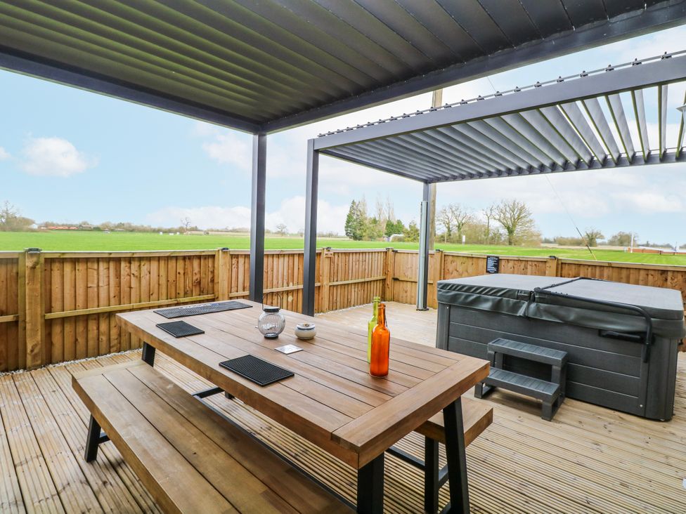 An outdoor patio with a table and hot tub at Aloe Lodge in Banham