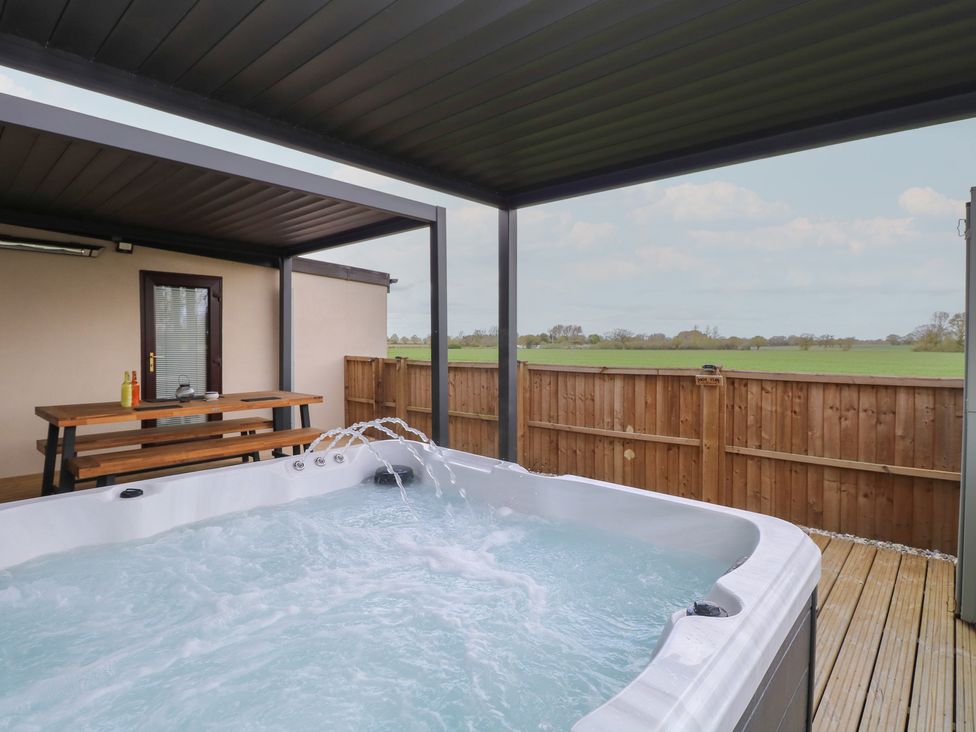 A hot tub with a wooden table in an outdoor area at Aloe Lodge in Banham