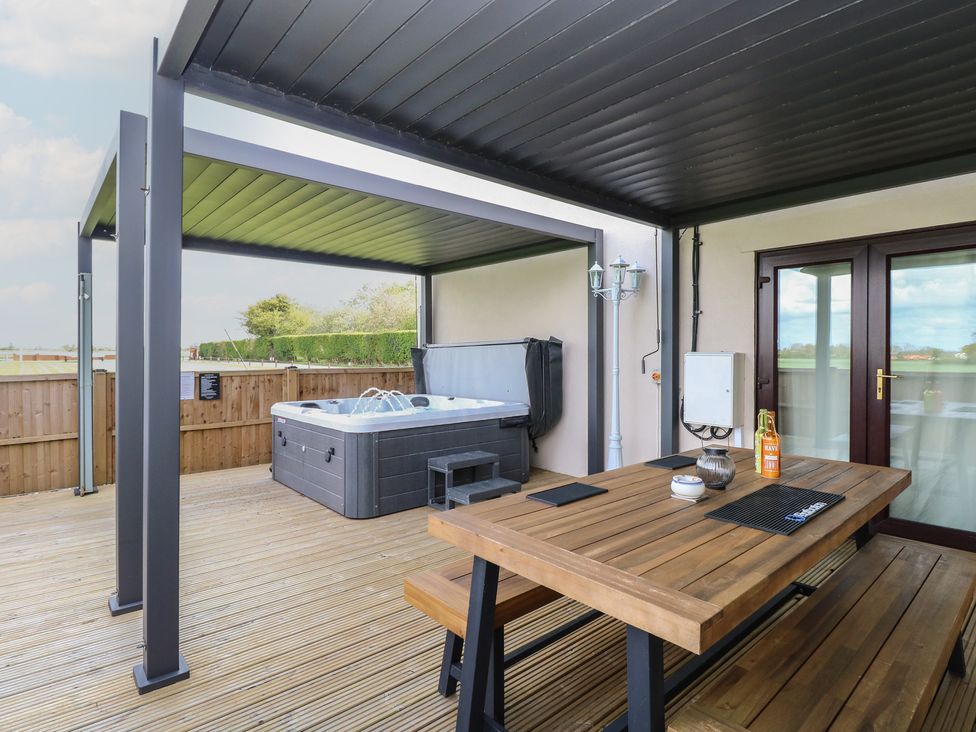 An outdoor seating area with a hot tub and wooden table at Aloe Lodge in Banham