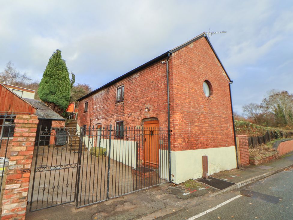 A brick house with a gate and trees at Quarry Barn in Wrexham
