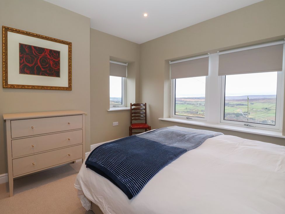 A bedroom with a bed, chest of drawers, and windows at Daisy Mount in Keighley