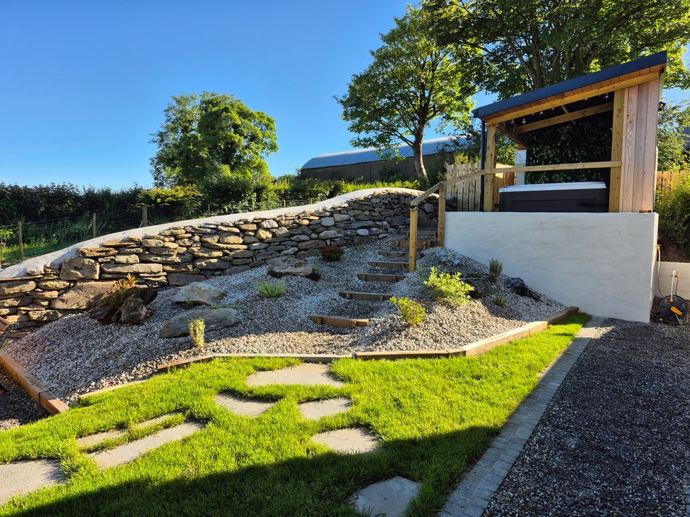 A garden with stone wall, steps, gravel, plants and a hot tub at Annie’s Farm Cottage near Londonderry, Northern Ireland