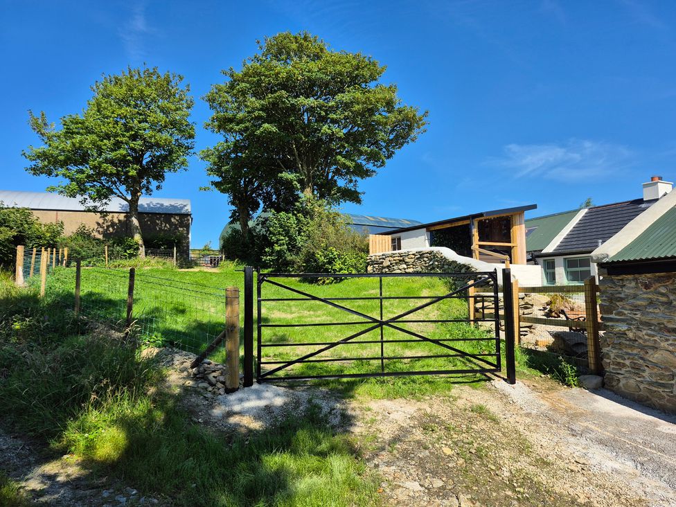 A gate leading to a grassy area with trees and a building at Annie’s Farm Cottage Near Londonderry, Northern Ireland