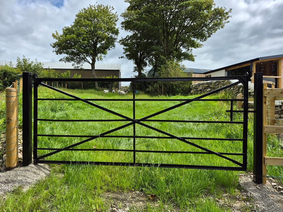 A gate leading to a grassy area with trees and a building at Annie’s Farm Cottage near Londonderry, Northern Ireland