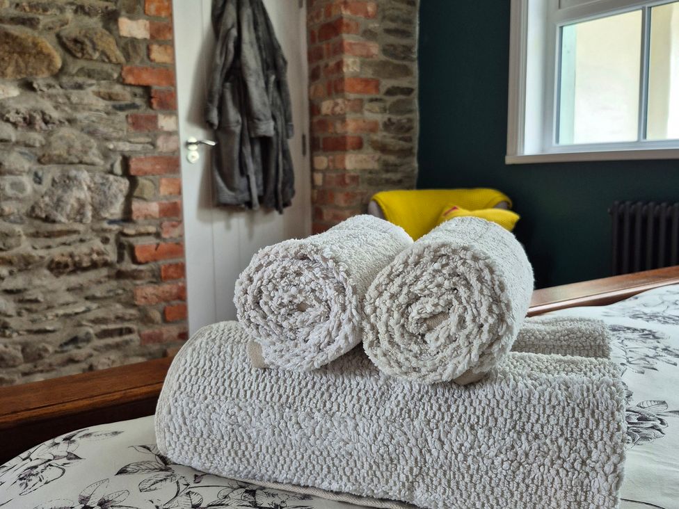 A stack of towels on a bed with a brick wall and a coat on a door at Annie’s Farm Cottage Near Londonderry, Northern Ireland