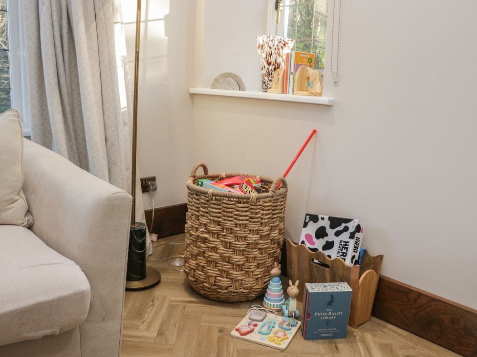 A living room corner with a basket of toys and children's books at North Cottage in Bowness-On-Windermere