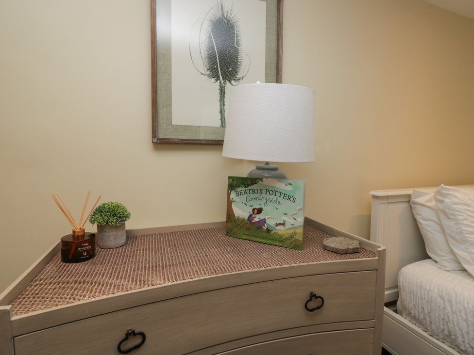 A dresser with a lamp, book, and decorative items at North Cottage Bowness-On-Windermere