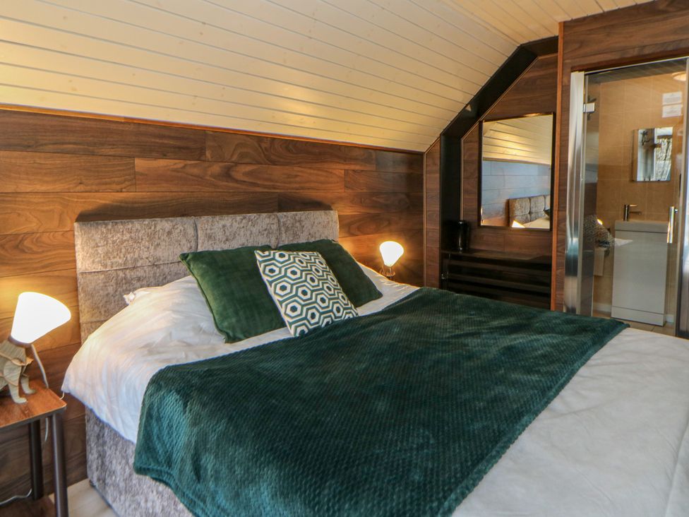 A bedroom with a bed, bedside lamp, and bathroom door at Garden Lodge 7 Swansea