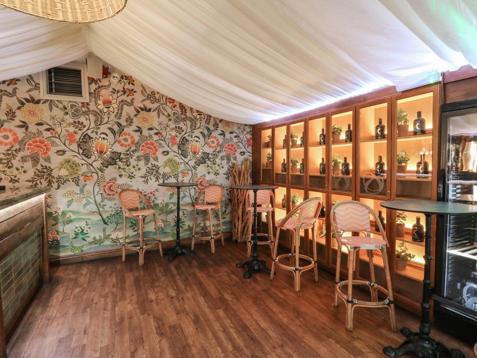 A bar area with stools and shelves displaying bottles at Garden Lodge 8 Swansea