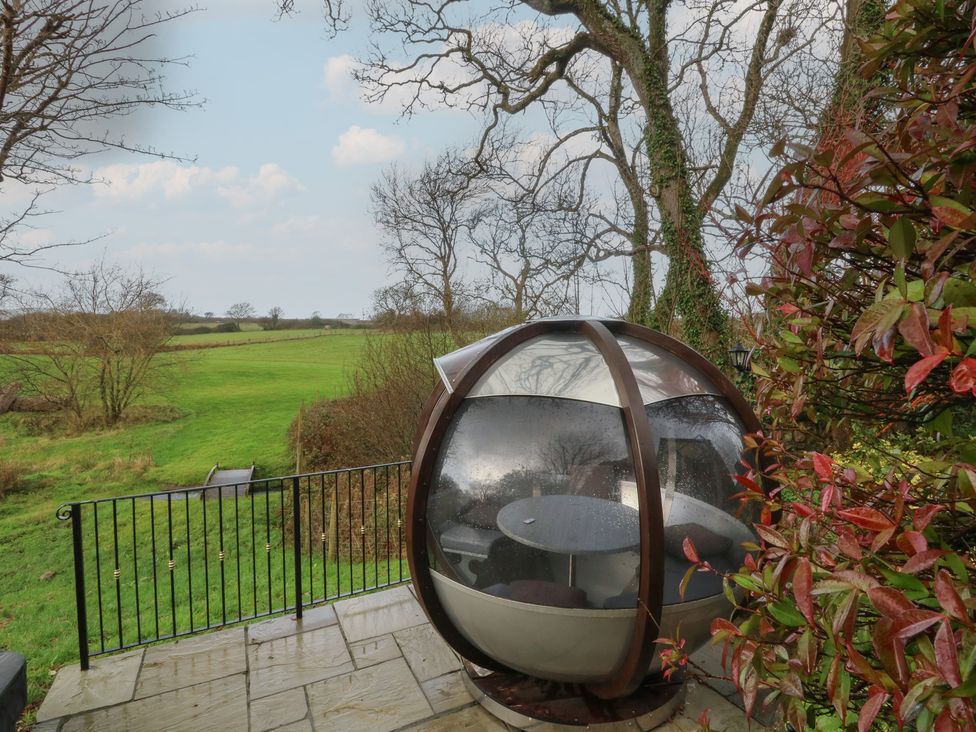 An outdoor seating pod with a table surrounded by grass and trees at Rose Apartment in Oldwalls near Reynoldston