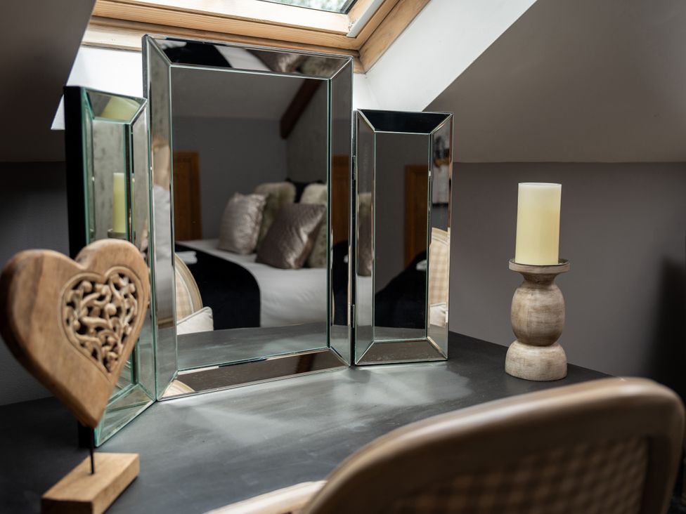 A mirror, candle and wooden heart on a table in a bedroom at Ivy Cottage Oldwalls near Reynoldston