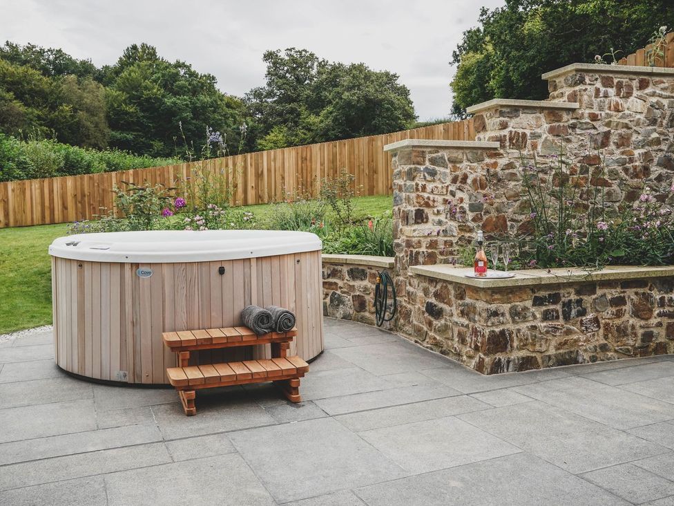 A garden with a hot tub and stone wall at Knowle House in Okehampton