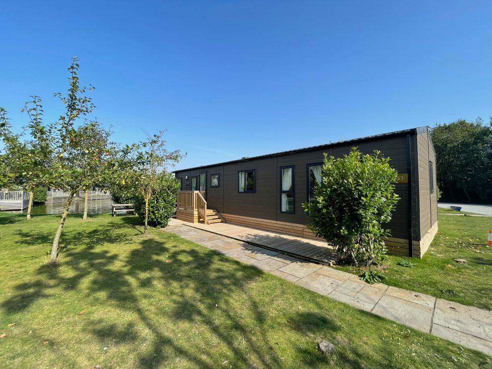 A mobile home with a deck and trees at Acacia Waterside Spa Carlton Miniott near Thirsk