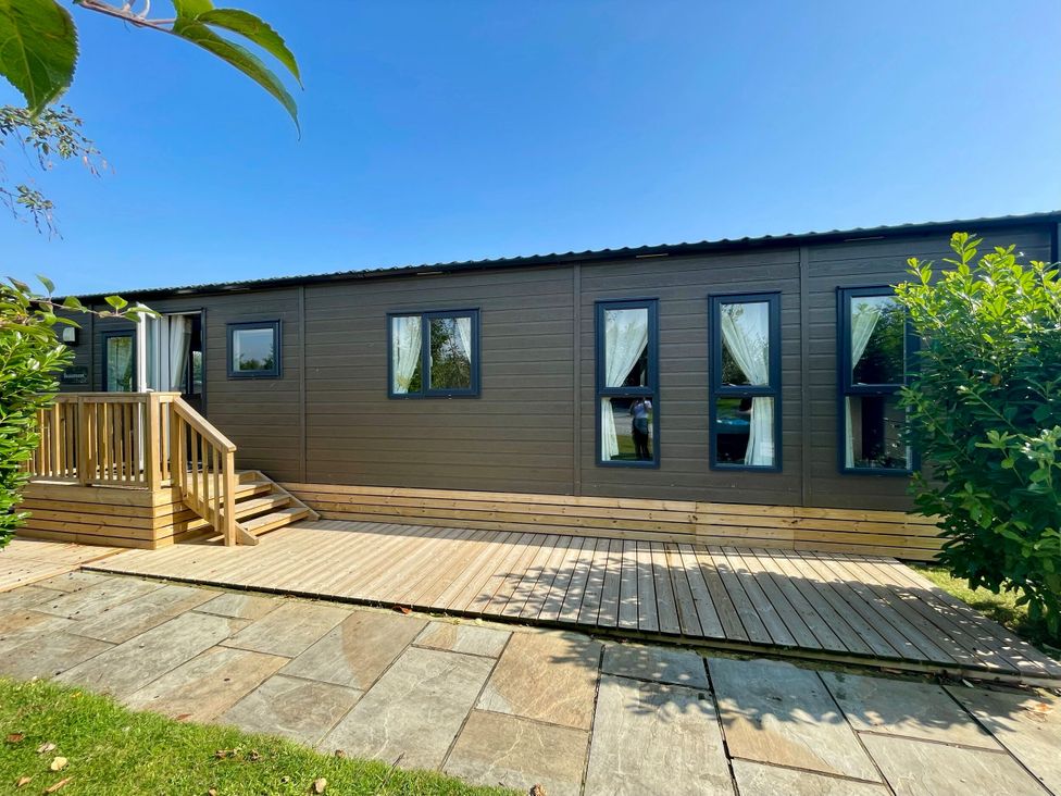 An exterior view of a cabin with a wooden deck at Acacia Waterside Spa Carlton Miniott near Thirsk