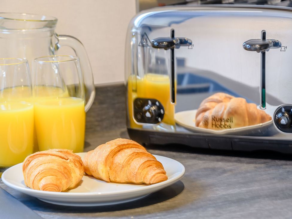 A kitchen countertop with a toaster, croissants, and glasses of orange juice at Cedar in Carlton Miniott near Thirsk