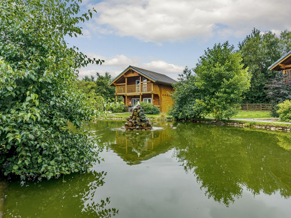 A house by a pond with trees and a fountain at Birch Waterside Spa in Carlton Miniott near Thirsk