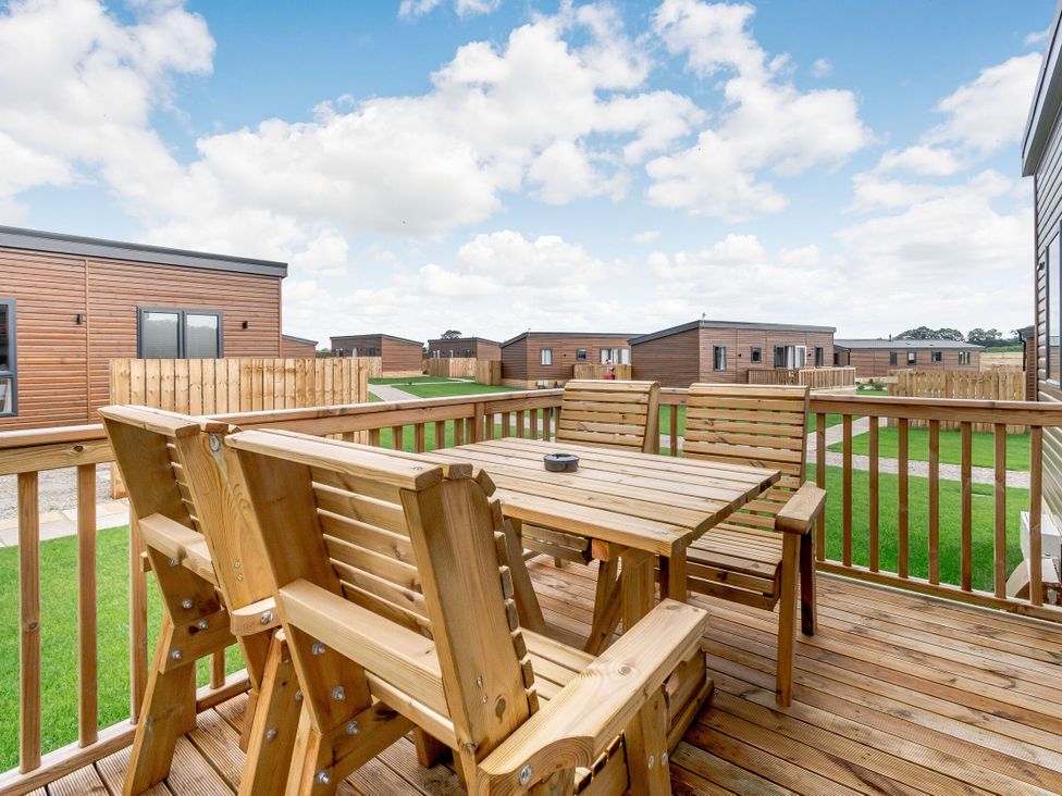 A patio area with a wooden table and chairs at Kinder Spa (Pet) Carlton Miniott near Thirsk