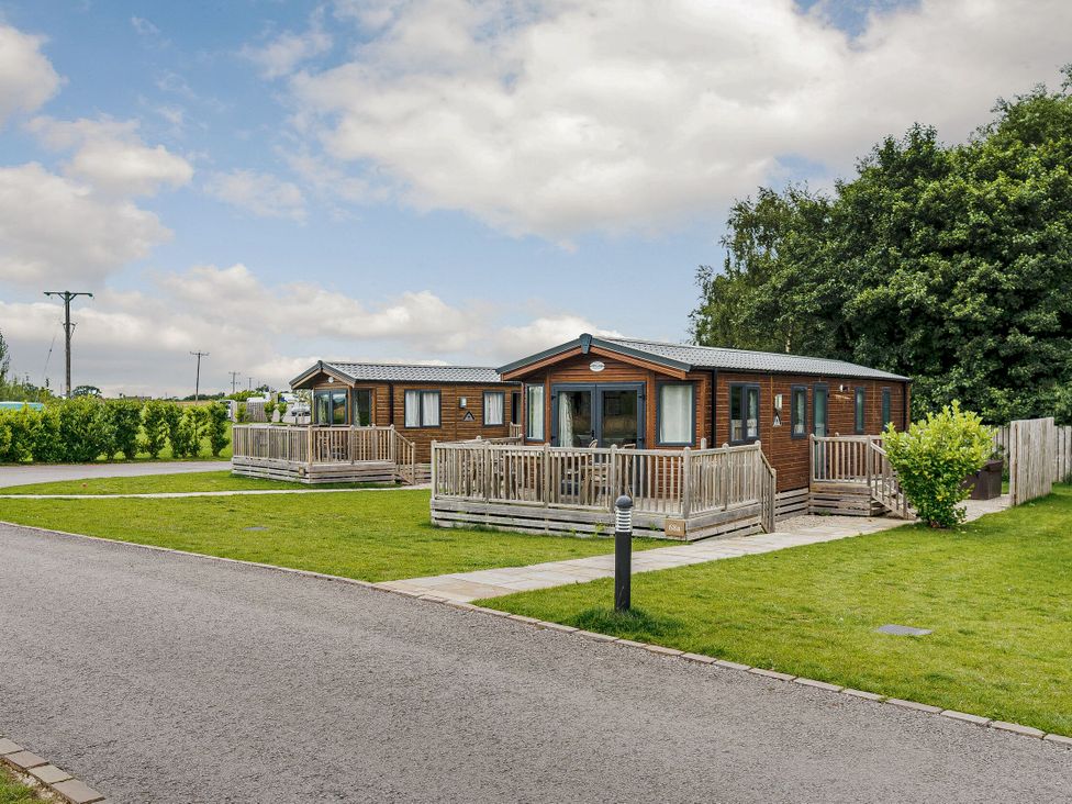 Two wooden cabins with decks in an outdoor area at Alder Spa (Pet) Carlton Miniott near Thirsk