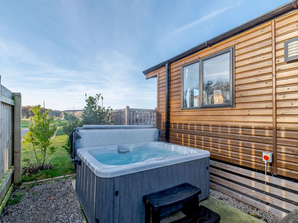 An outdoor area with a hot tub beside a wooden cabin at Alder Spa (Pet) Carlton Miniott near Thirsk