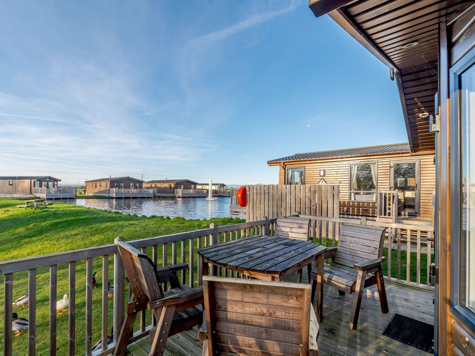 An outdoor area with a wooden table and chairs near the water at Alder Waterside Spa (Pet) Carlton Miniott near Thirsk