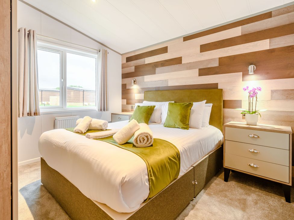 A bedroom with a bed and nightstand at Oak Waterside Spa Carlton Miniott near Thirsk
