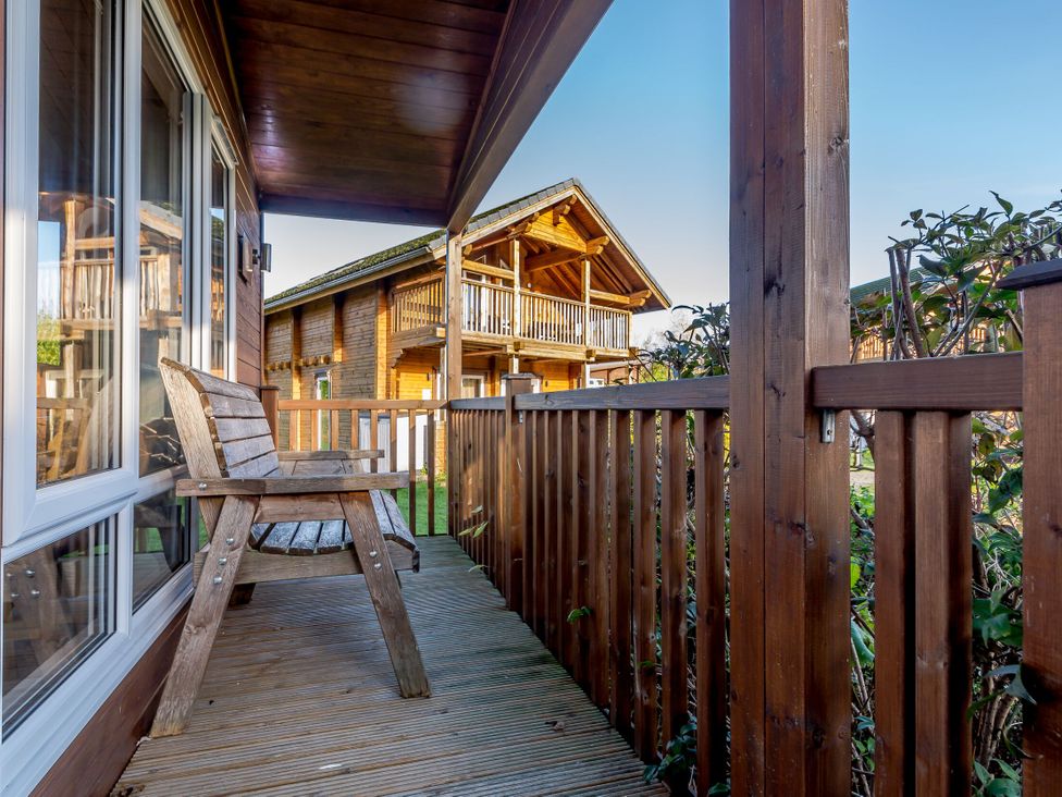 A balcony with a wooden chair and view of cabins at Fir Tree Waterside Spa Carlton Miniott near Thirsk