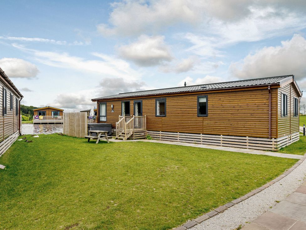 An outdoor view of a log cabin with a deck at Larch Waterside Spa Carlton Miniott near Thirsk