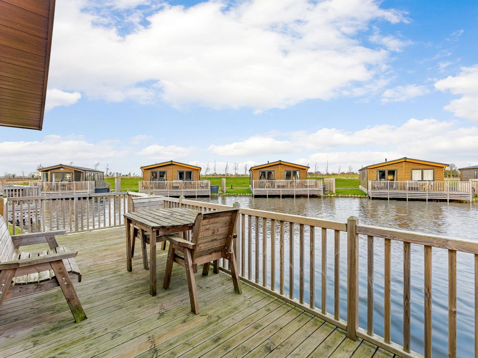 An outdoor area with a wooden table and chairs near water at Larch Waterside Spa Carlton Miniott near Thirsk